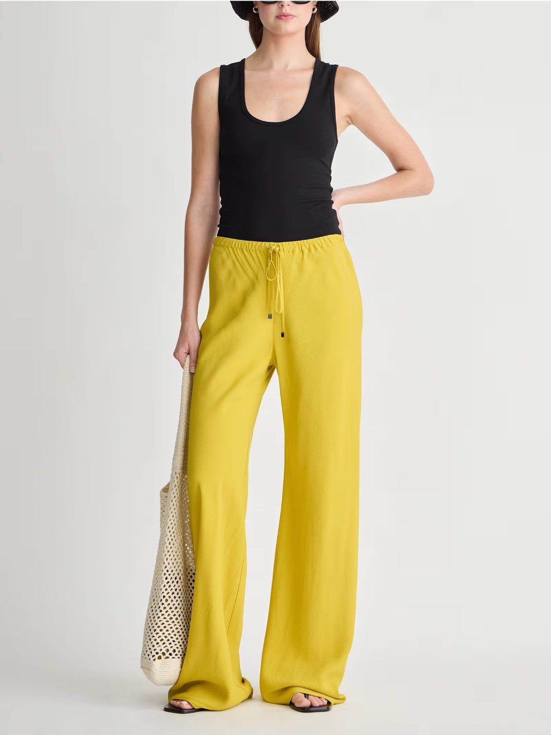 Woman wearing a black sleeveless top and yellow pants on a white background