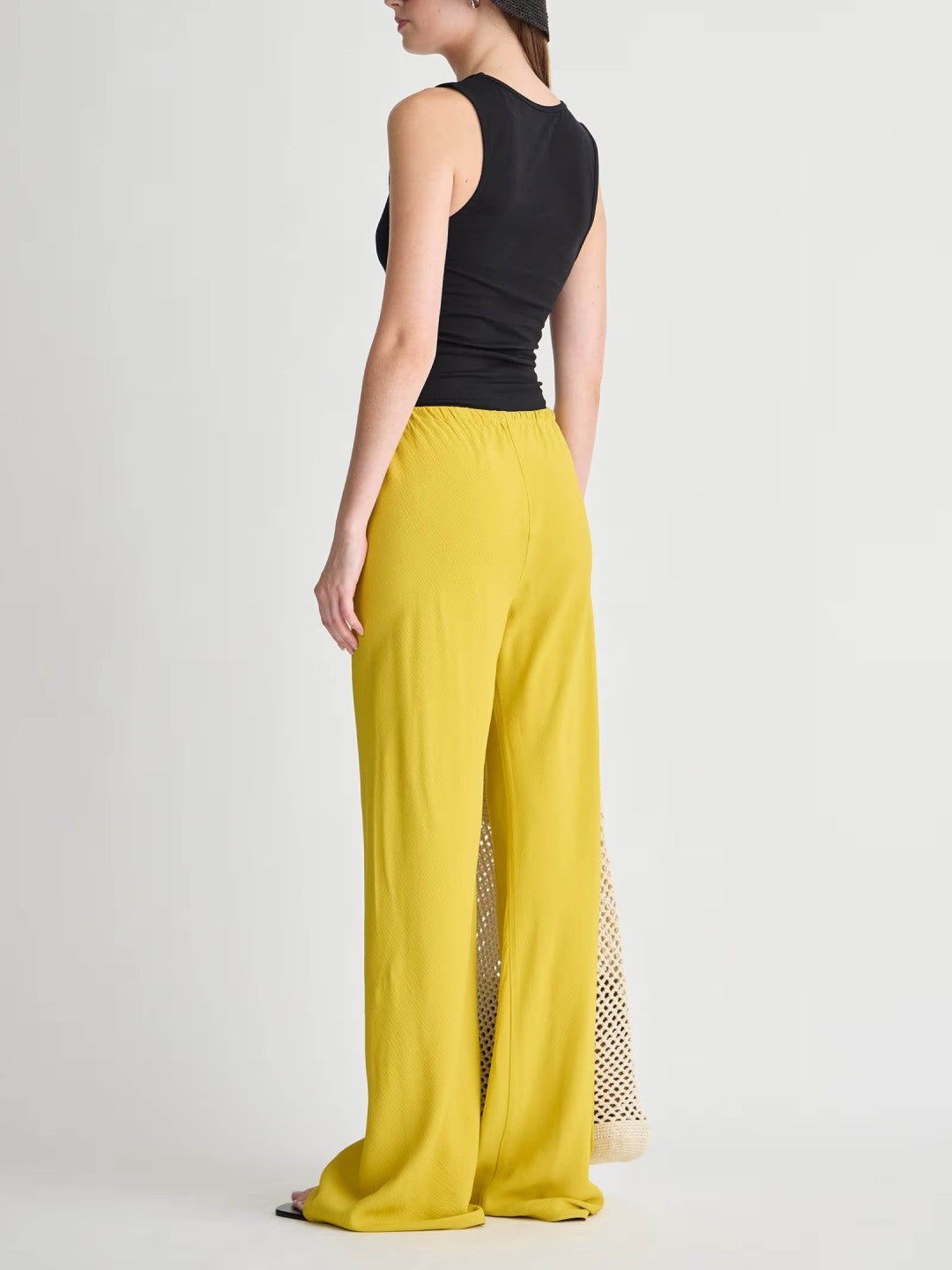 Person wearing a black sleeveless top and yellow pants with a subtle pattern on a white background