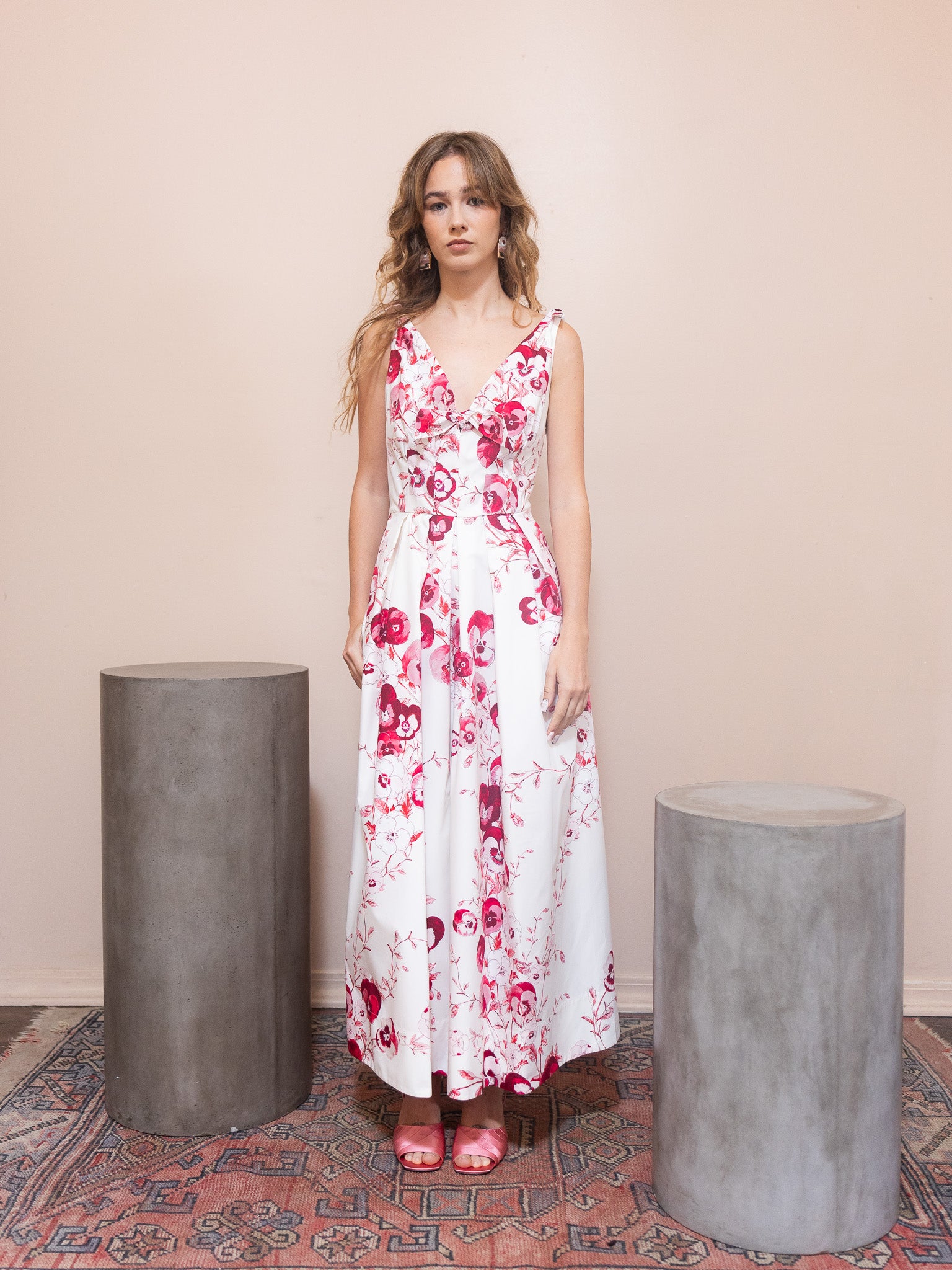 Woman in a floral dress standing between two cylindrical concrete planters against a beige wall.