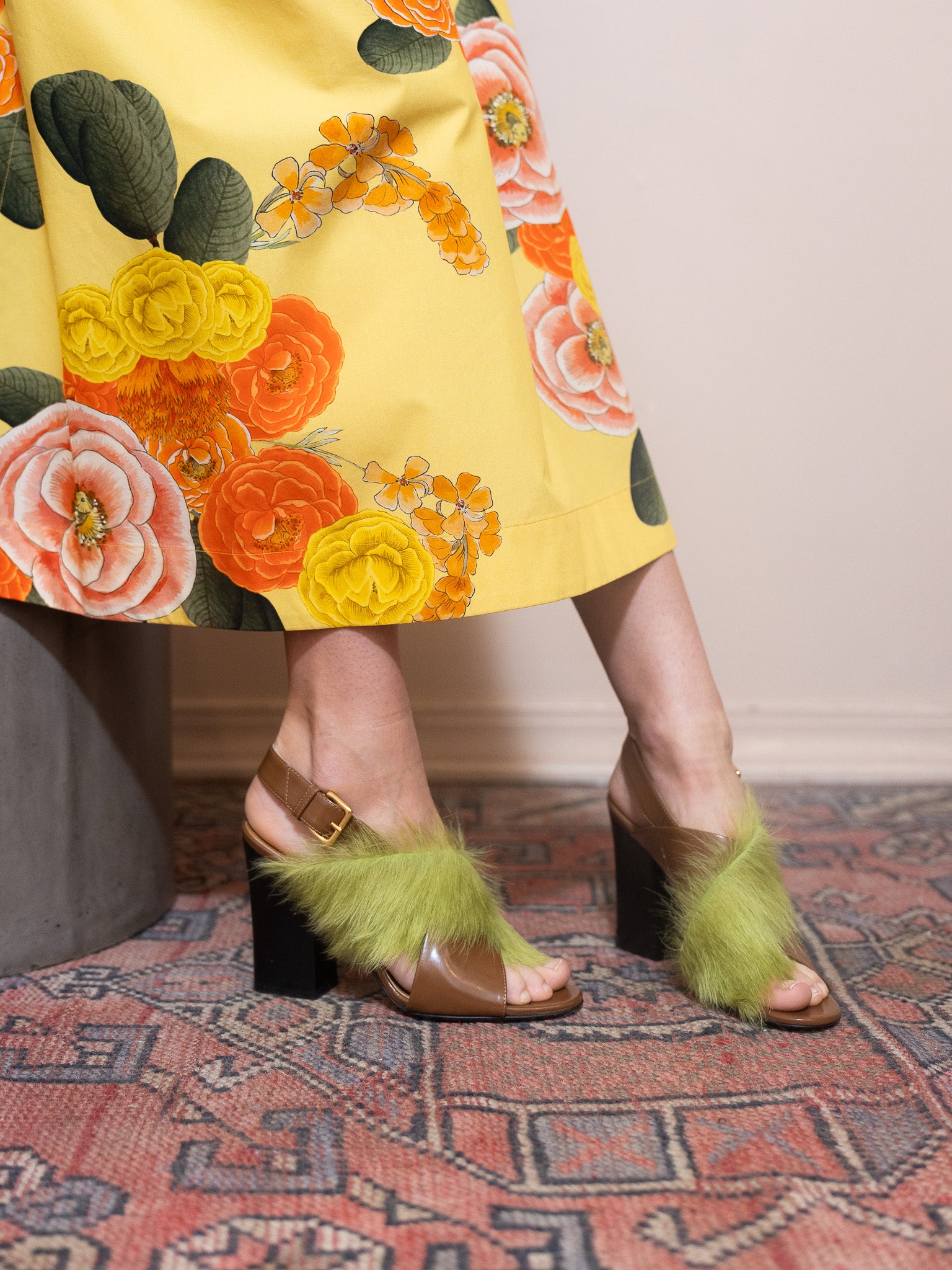 Person wearing a floral dress and green furry heels on a patterned rug.