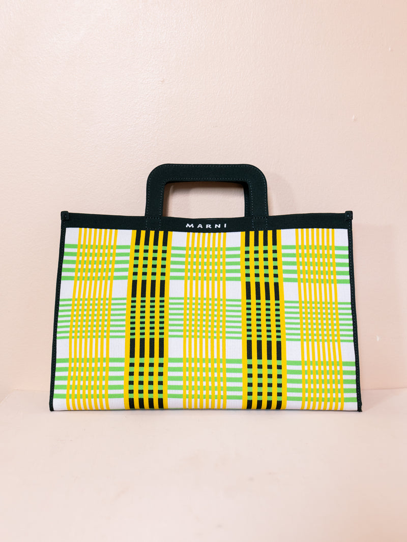 Green, yellow, and black plaid bag against pink background.