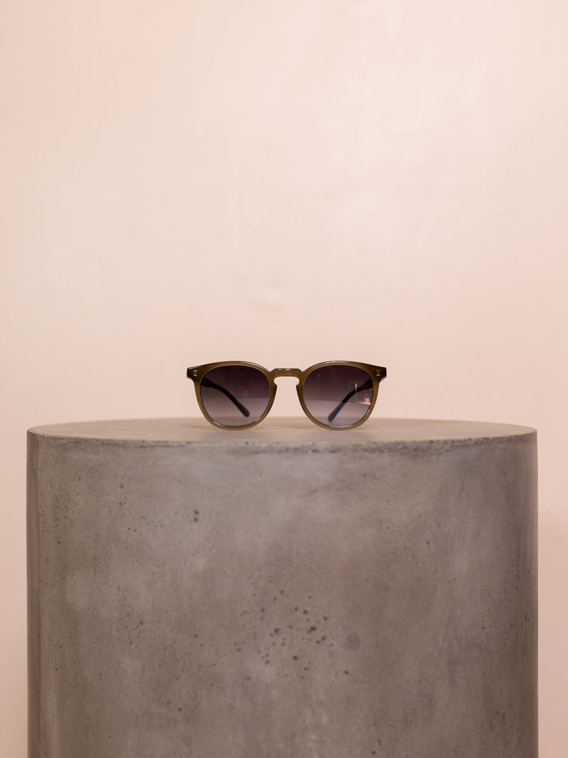 Green round sunglasses on pedestal against pink background.