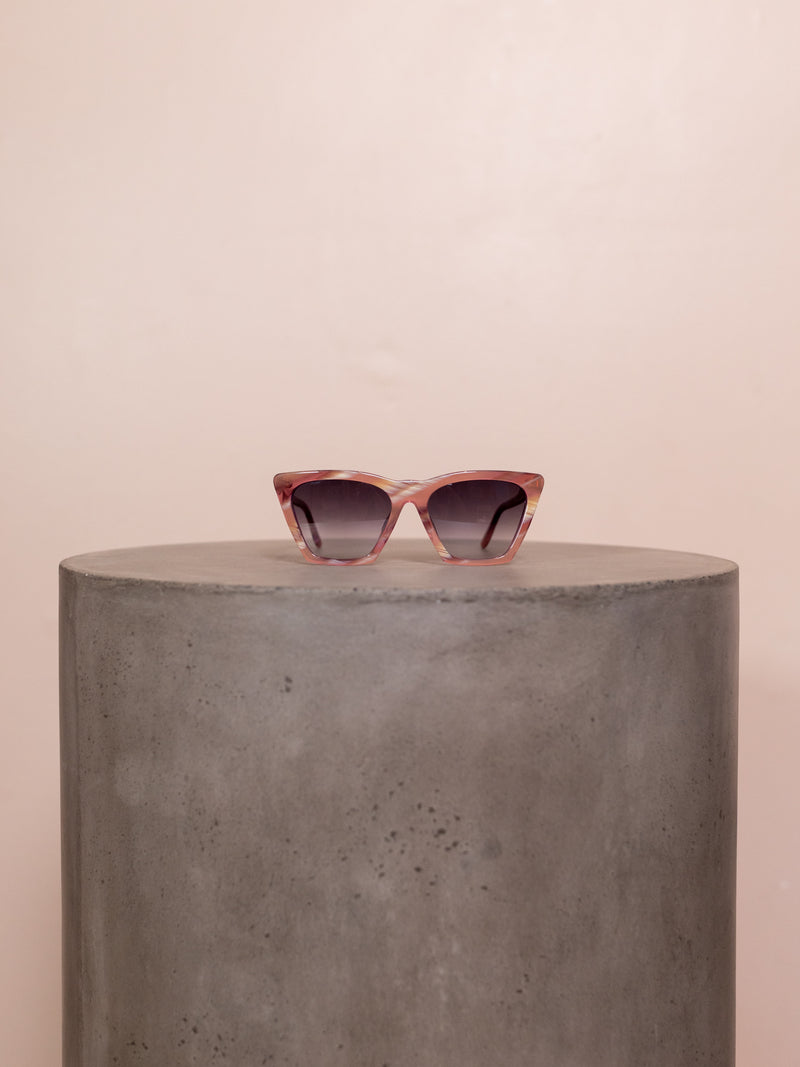 Pink angular sunglasses on pedestal against pink background.