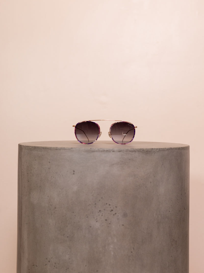 Wire framed sunglasses on pedestal against pink background