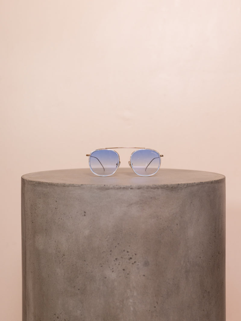 Blue wire frame sunglasses on pedestal against pink background.