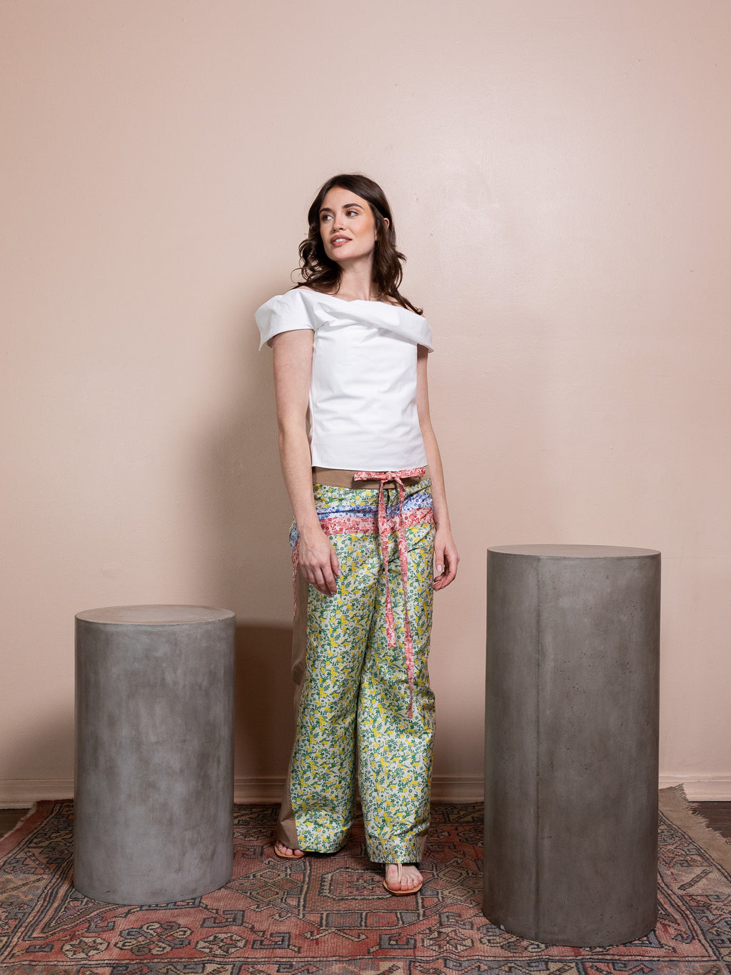 Woman in white top and floral pants against pink background