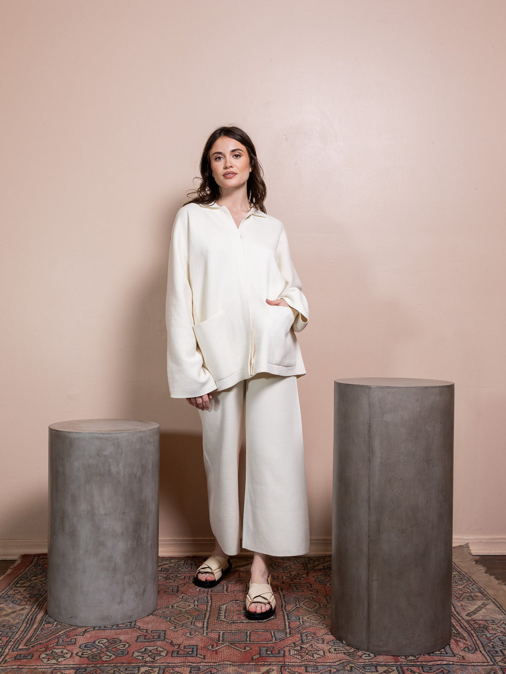 Woman in white sweater and white pants against pink background