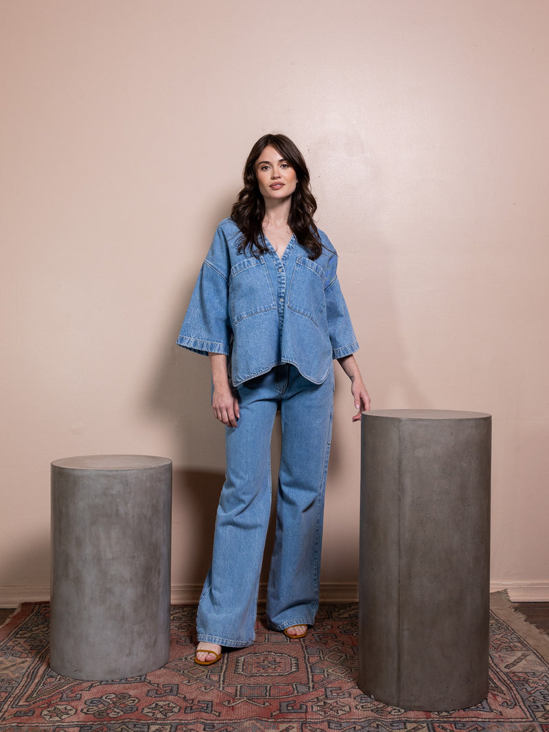 Woman in denim button up and blue jeans against pink background