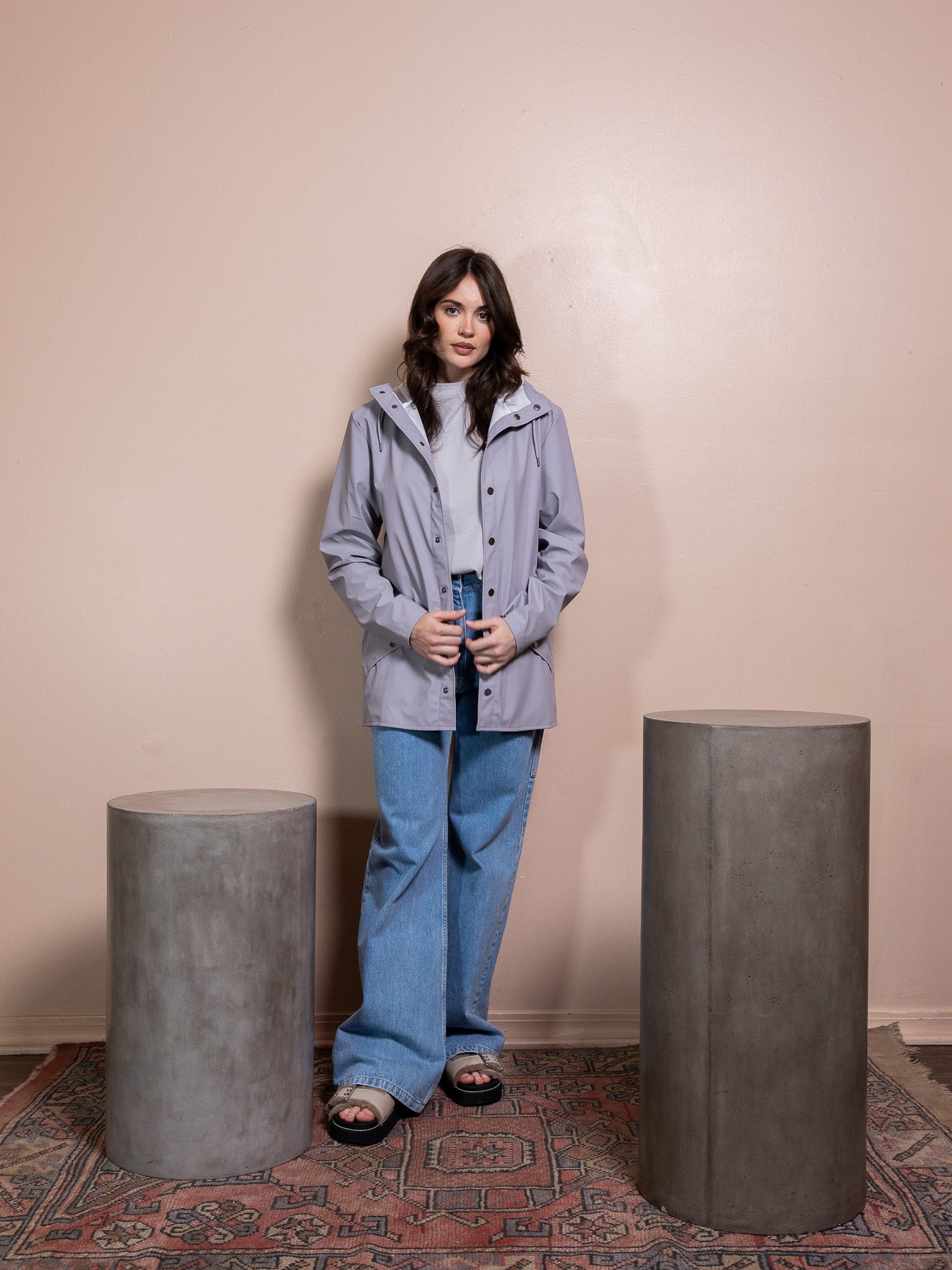 Woman in purple rain jacket and blue jeans against pink background