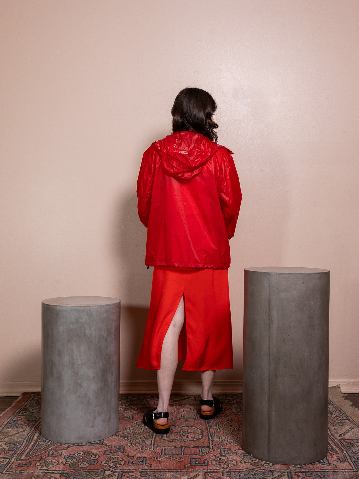 Woman in red dress and red rain jacket against pink background