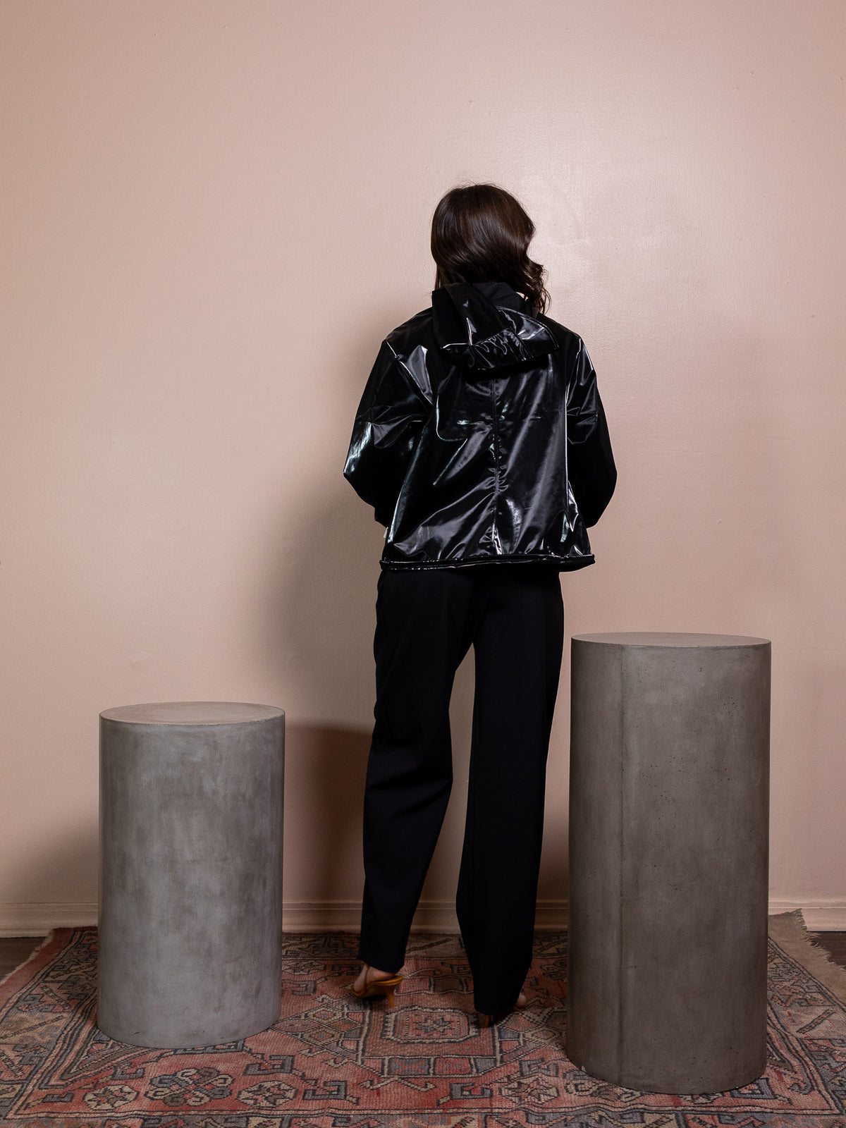 Woman in white top, black rain jacket, and black pants against pink background