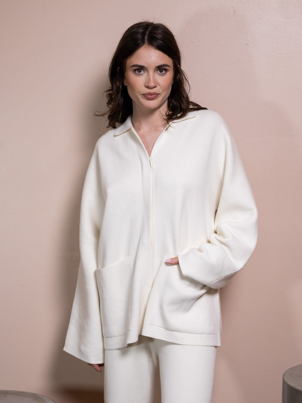 Woman in white sweater and white pants against pink background