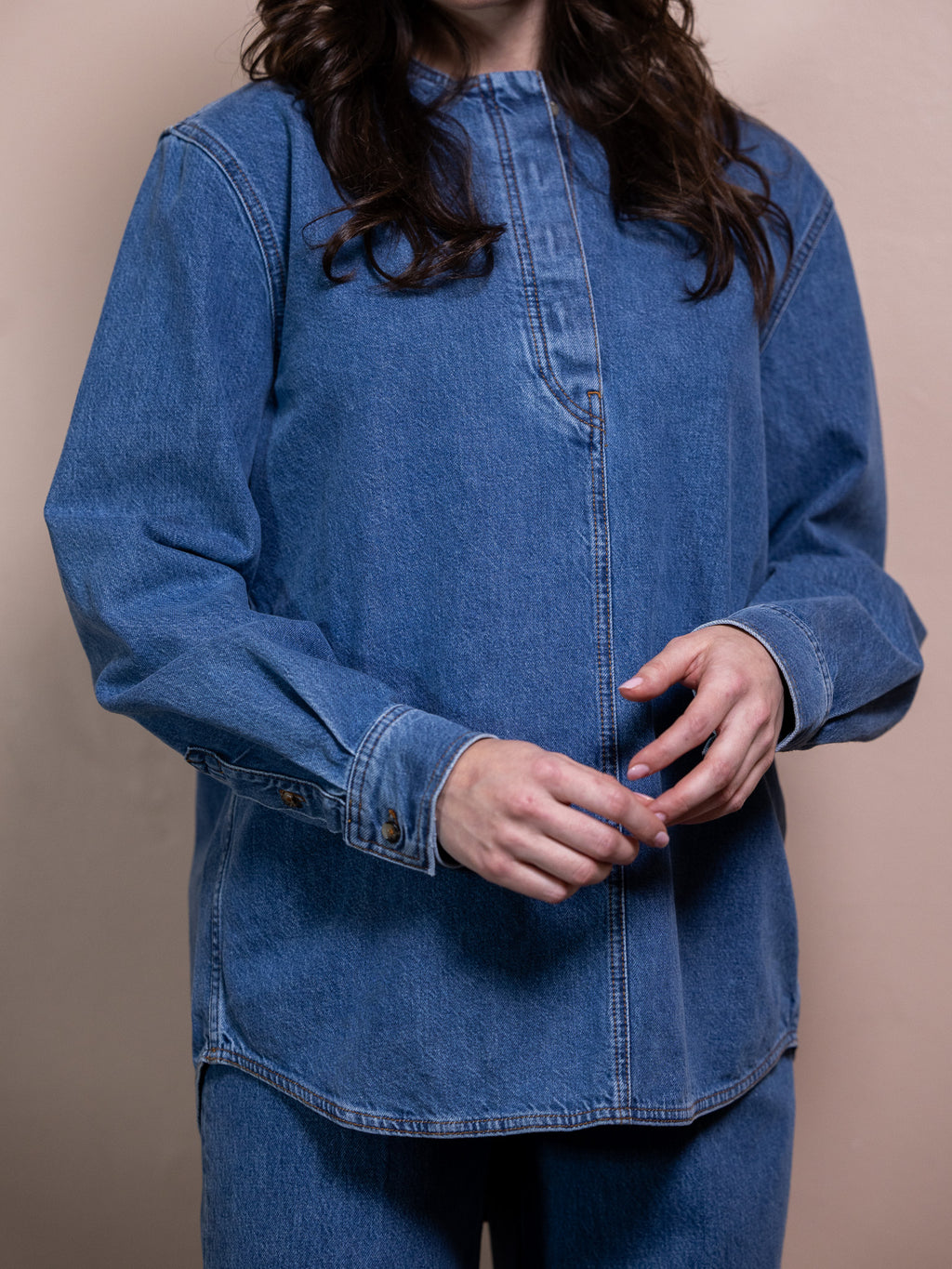 Woman in blue denim shirt and blue jeans against pink background