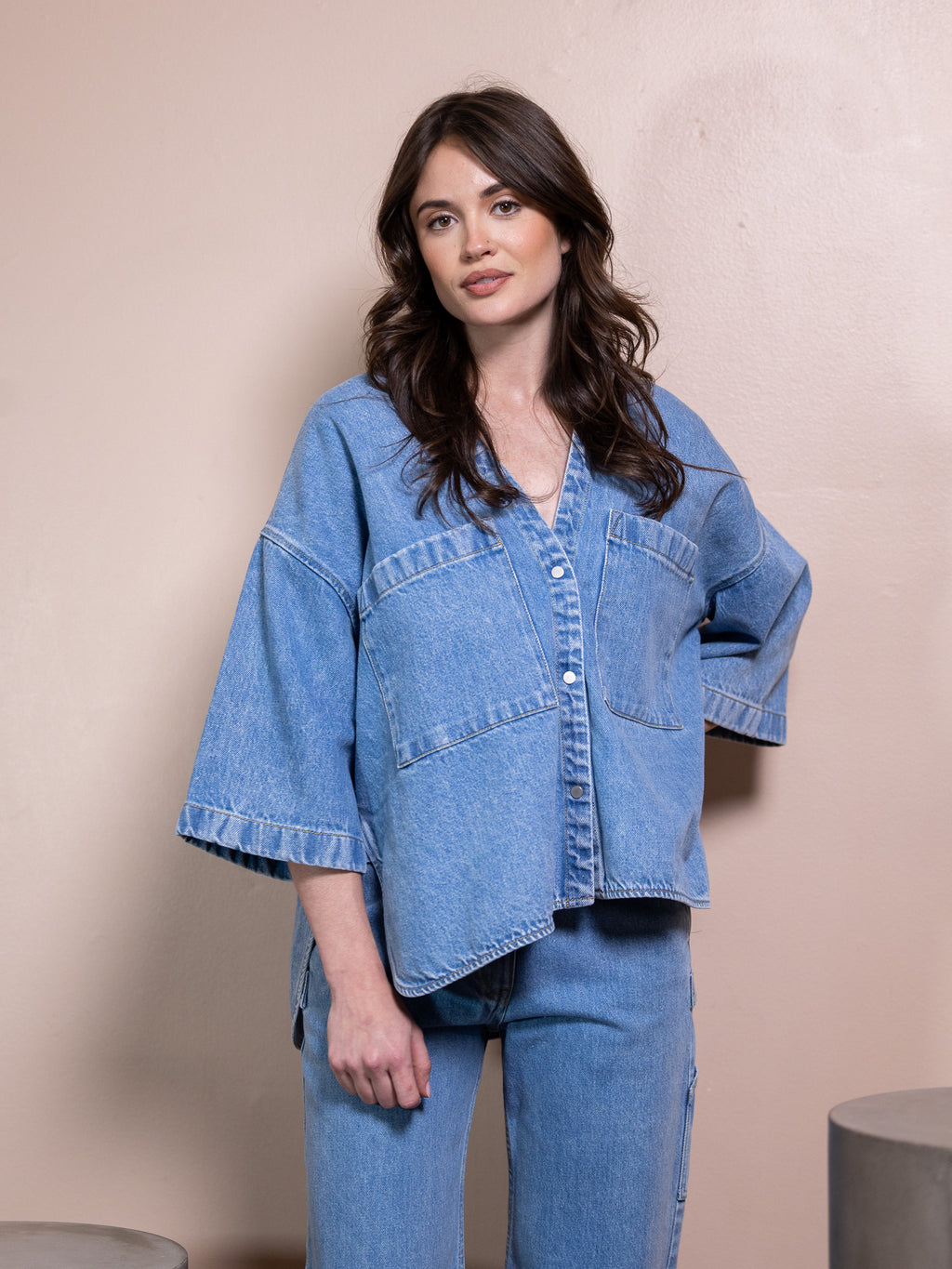 Woman in denim button up and blue jeans against pink background