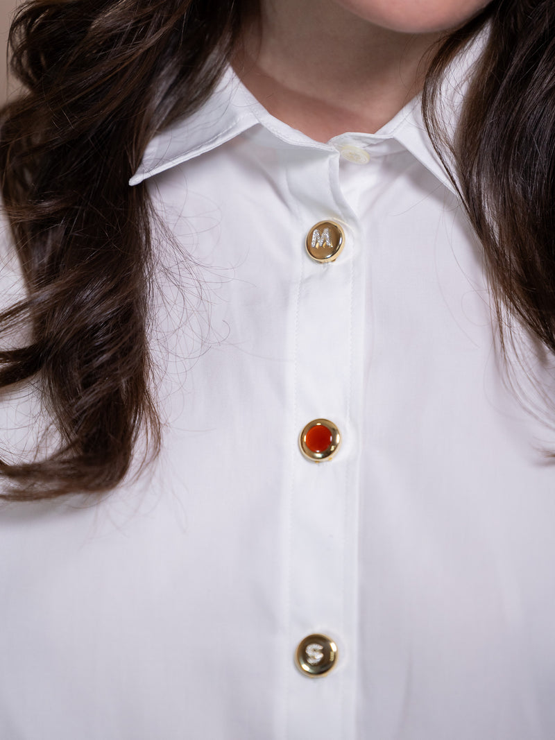 Gold button cover with diamond M on white shirt.