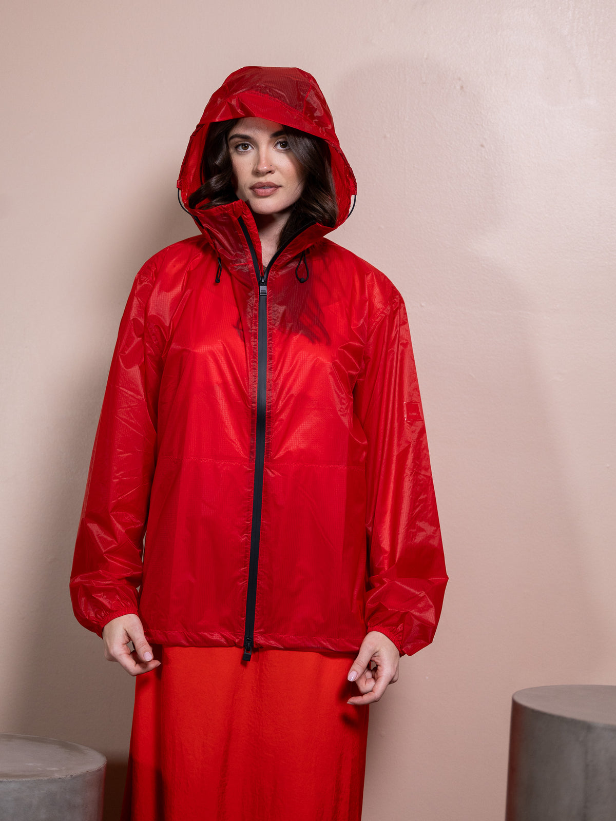 Woman in red dress and red rain jacket against pink background