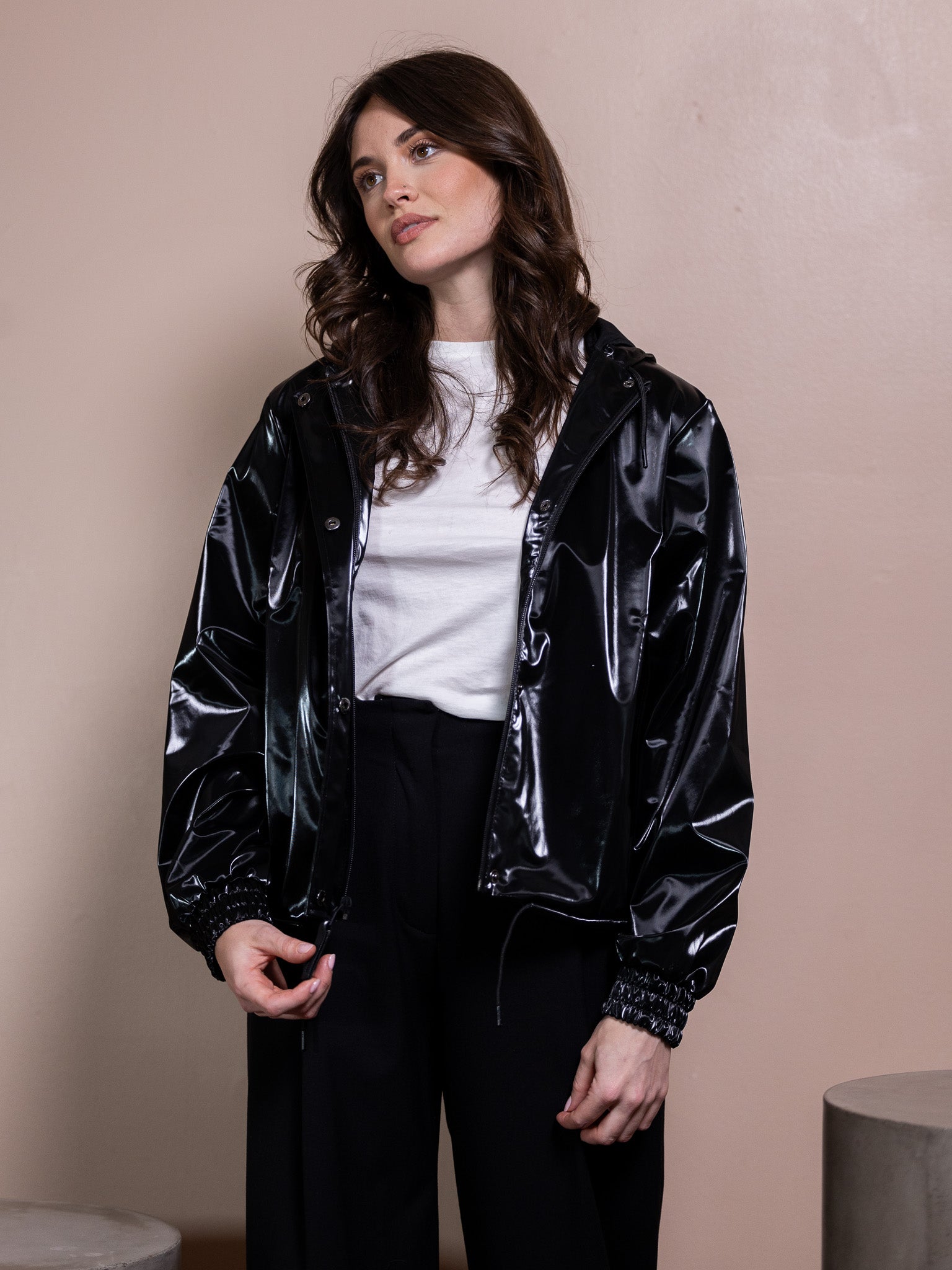 Woman in white top, black rain jacket, and black pants against pink background