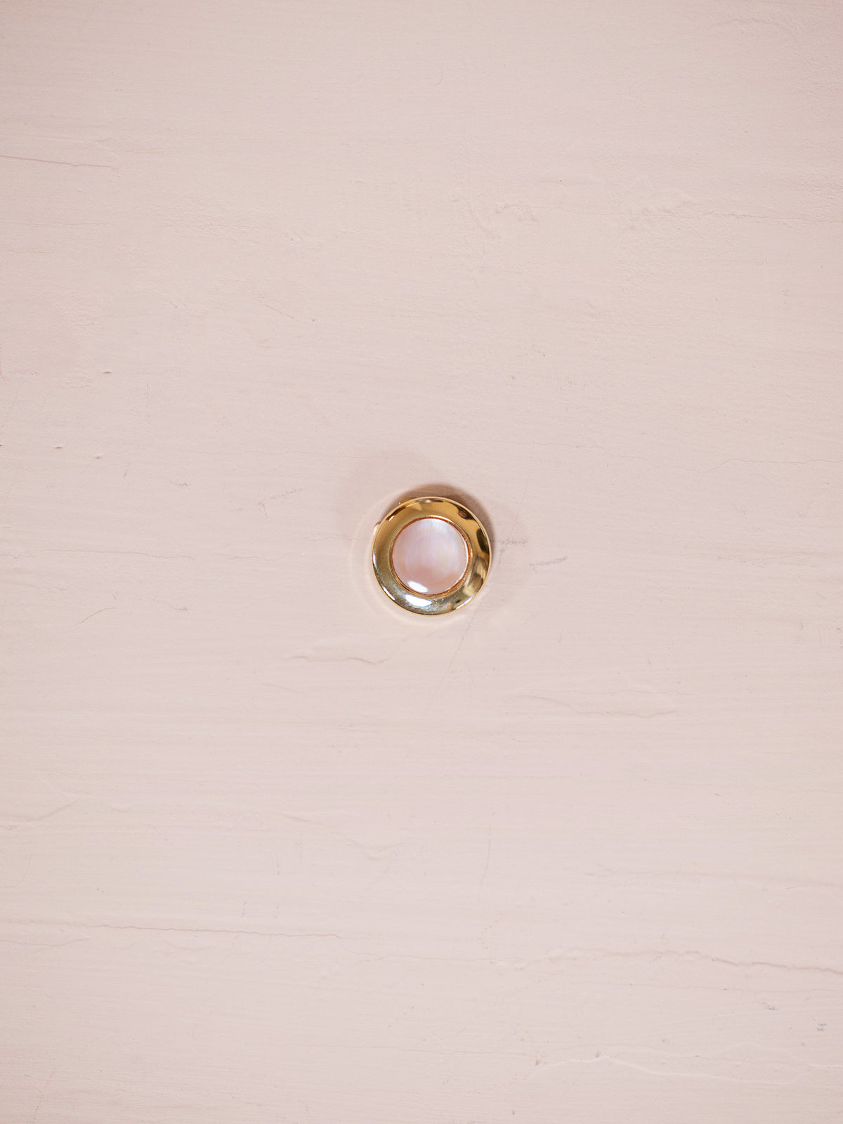 Pink mother of pearl and gold button cover on pink background.