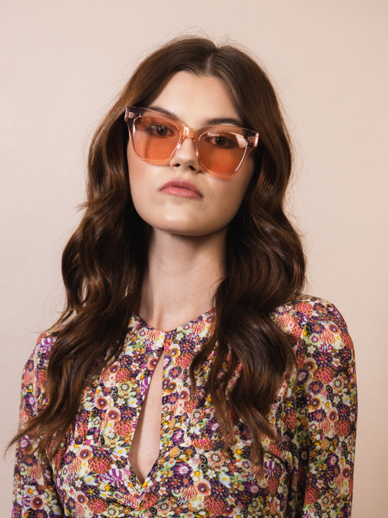Woman wearing sunglasses. The sunglasses have clear pink frames with a pink tint and pink lenses. CHIMI 07 Pink.
